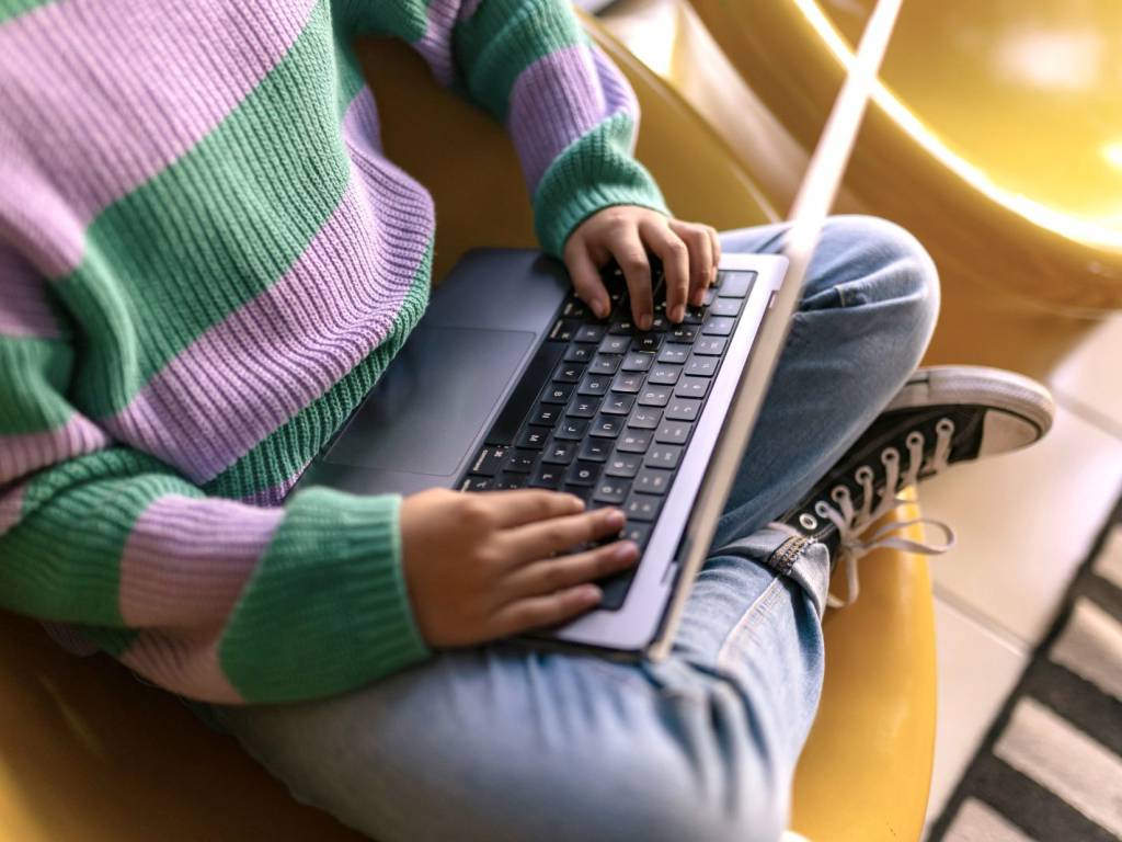 En ungdom sitter i en stol med laptop i fanget. Aansiktet til personen vises ikke. (Foto)