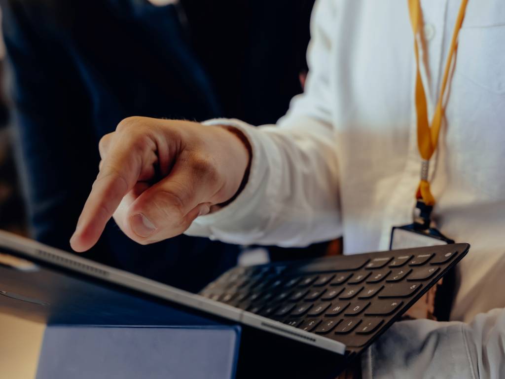 En mann peker på skjermen til laptopen han holder i hånda. Ansiktet til mannen er ikke synlig. (Foto)